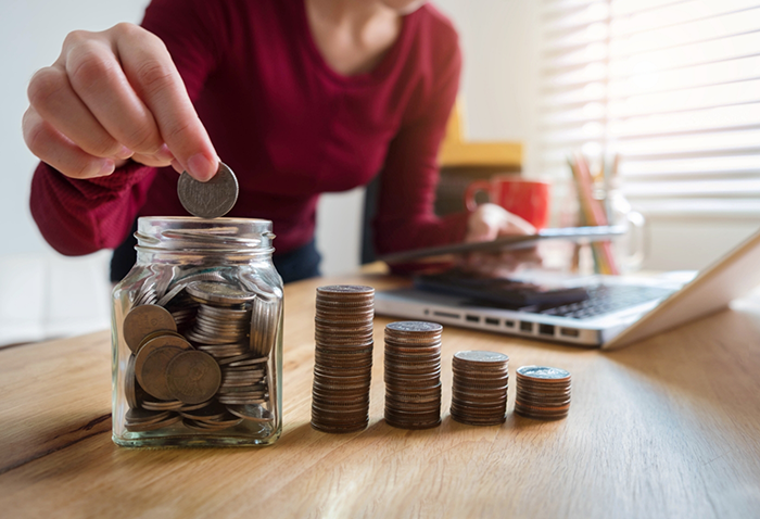 Woman placing coins into a jar while typing on a laptop