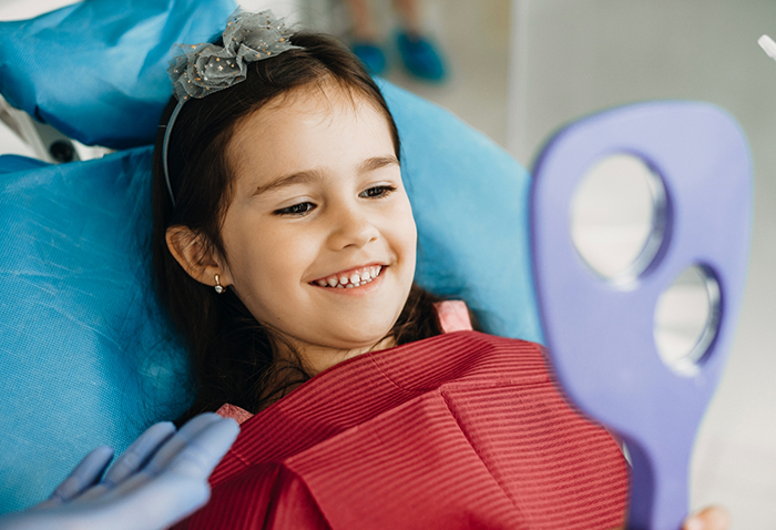 Young girl in the dental chair looking at her smile in a mirror