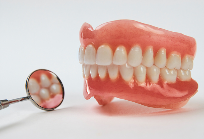 Set of full dentures next to a dental mirror