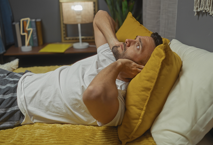Man laying awake in bed and holding the sides of his jaw