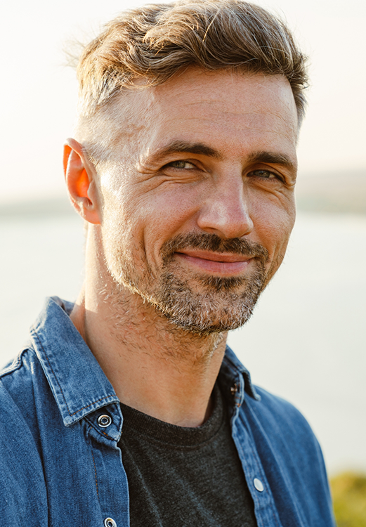 Man in a denim shirt smiling outdoors