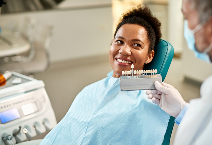 Woman smiling while a dentist holds a shade guide in front of her teeth