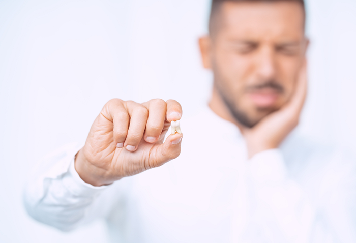 Man holding his cheek in pain with one hand and holding his extracted tooth in the other